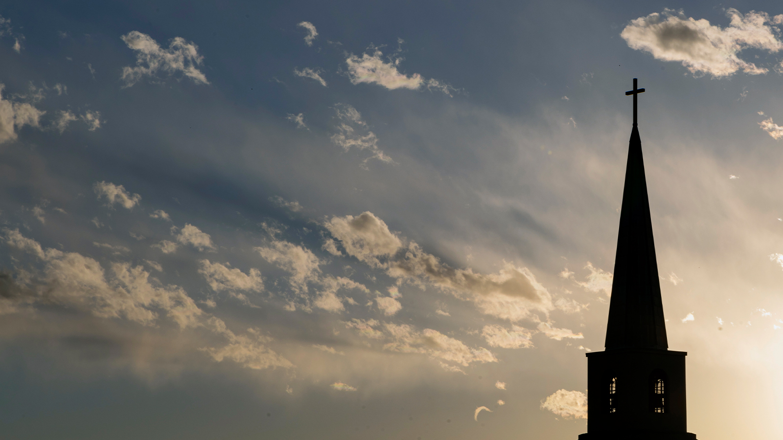 Church steeple with a cross with cloudy, blue sky in background. 