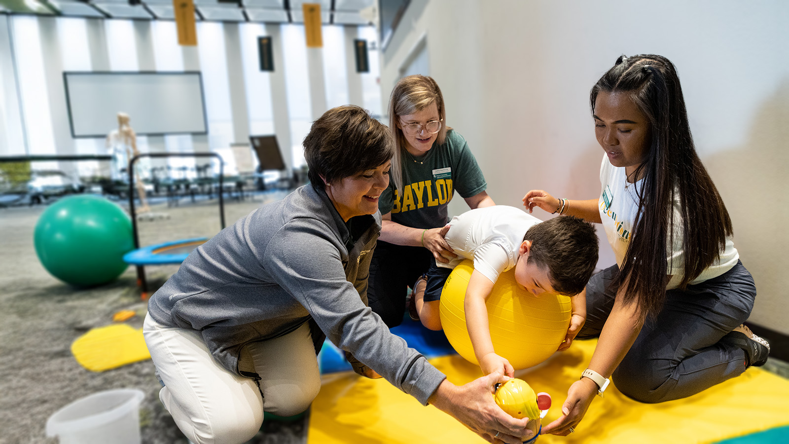Occupational therapy students and faculty work with a child using an exercise ball and Mr Potato Head toy.