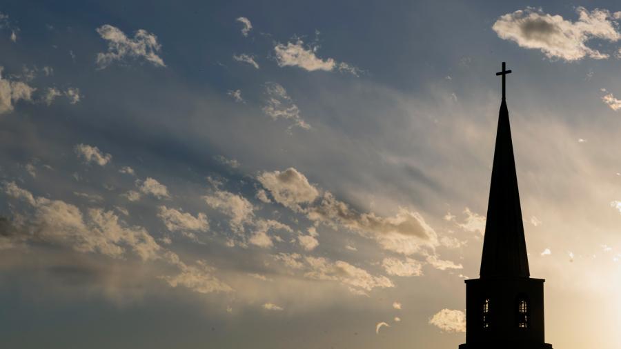 Church steeple with a cross with cloudy, blue sky in background. 