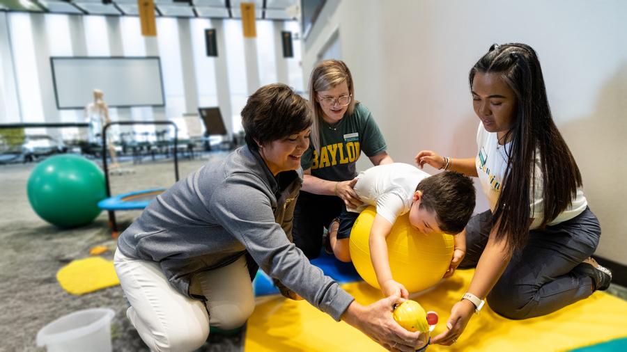 Occupational therapy students and faculty work with a child using an exercise ball and Mr Potato Head toy.
